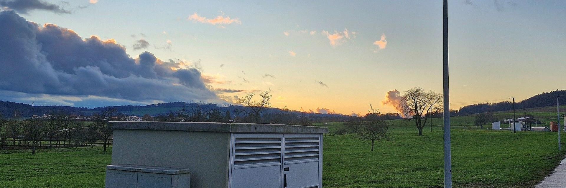 Eine Transformatorenstation steht auf einem saftigen, grünen Feld, das mit Gras bewachsen ist.