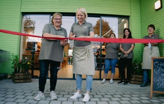 Zwei Mitarbeiterinnen durchtrennen symbolisch das Eröffnungsband des Dorfladens